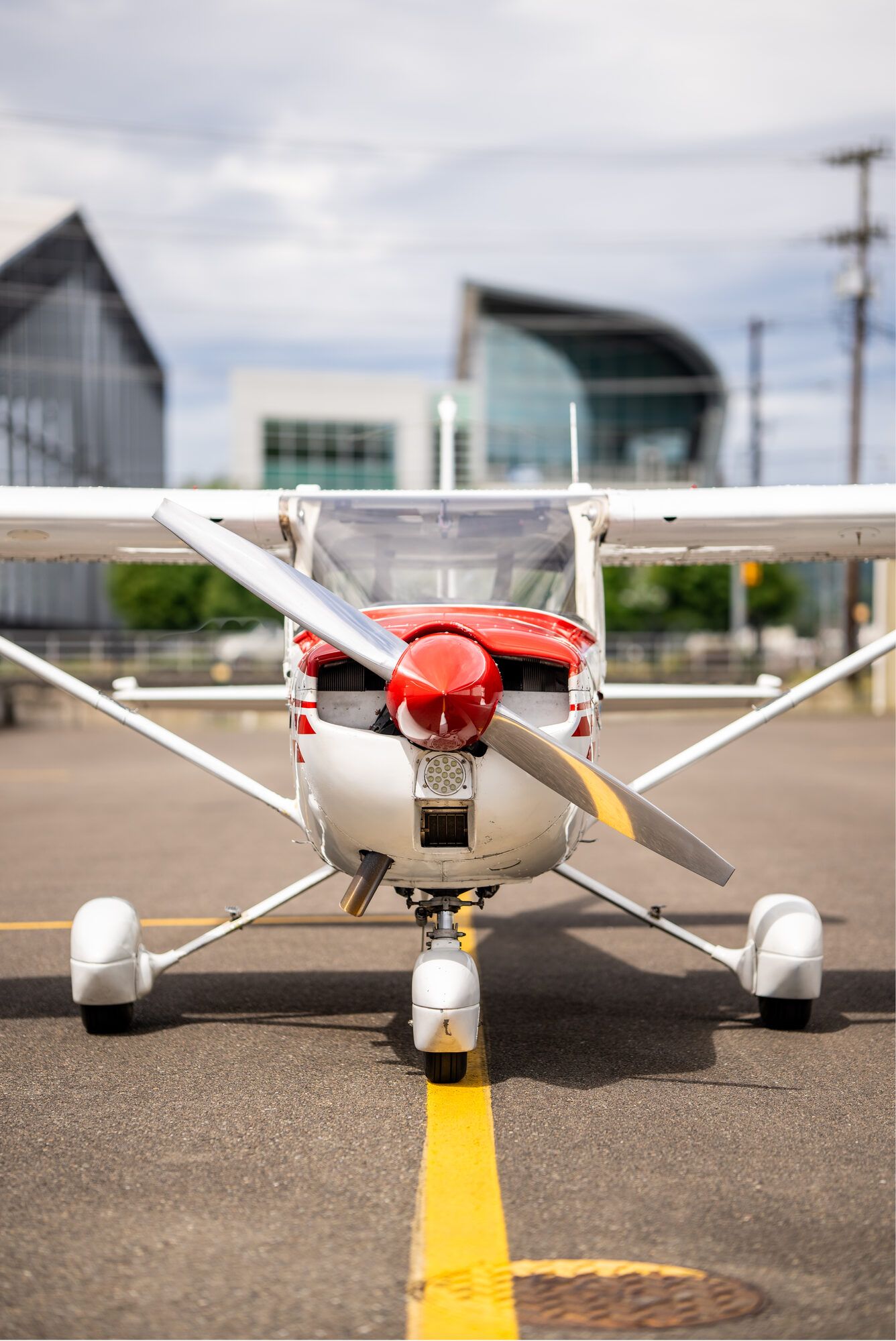 Cessna 150M head on, red spinner and cowl, on a ramp with a building behind
