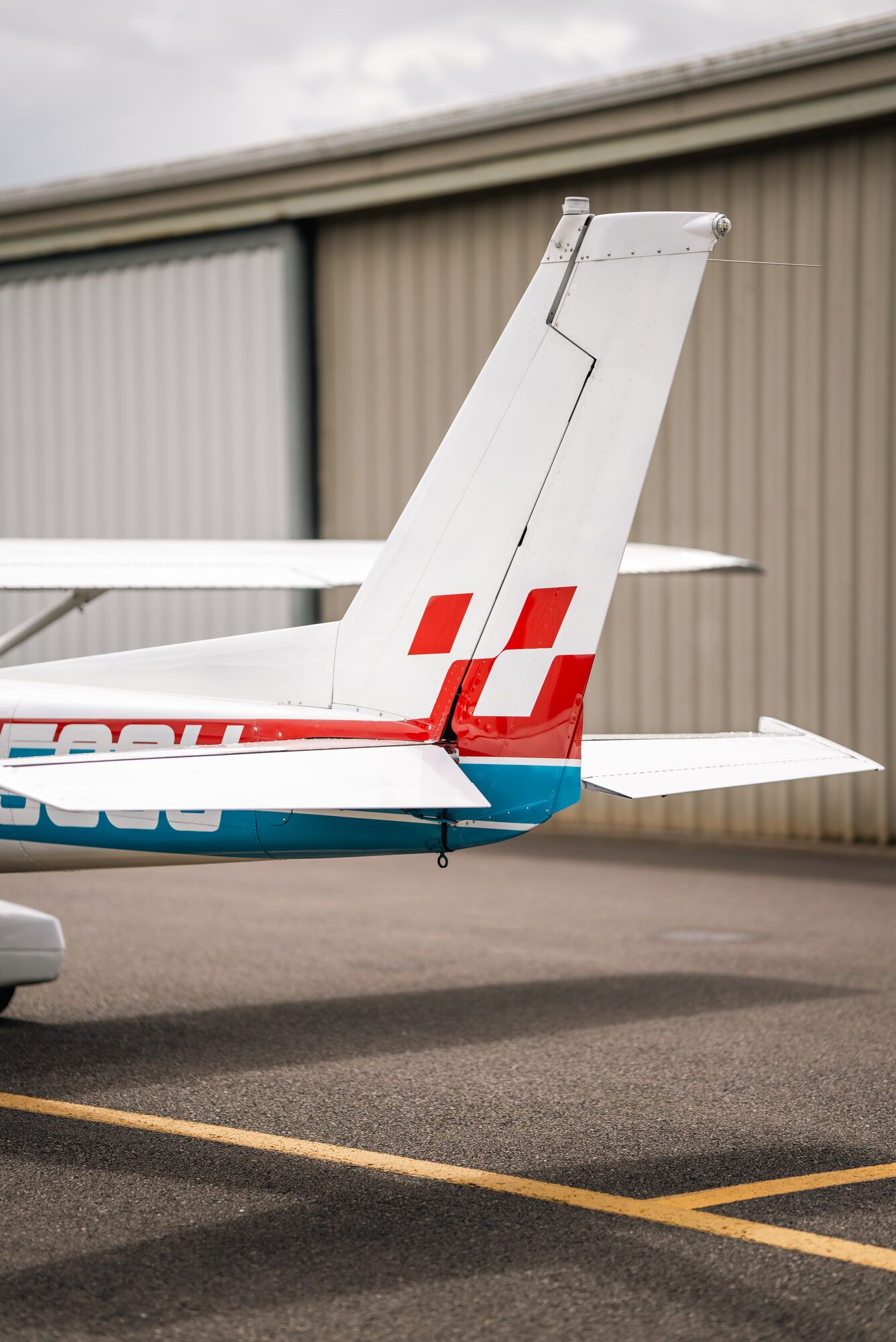 Cessna 150M tail with the red checkerboard rudder and blue stripe, beside a hangar