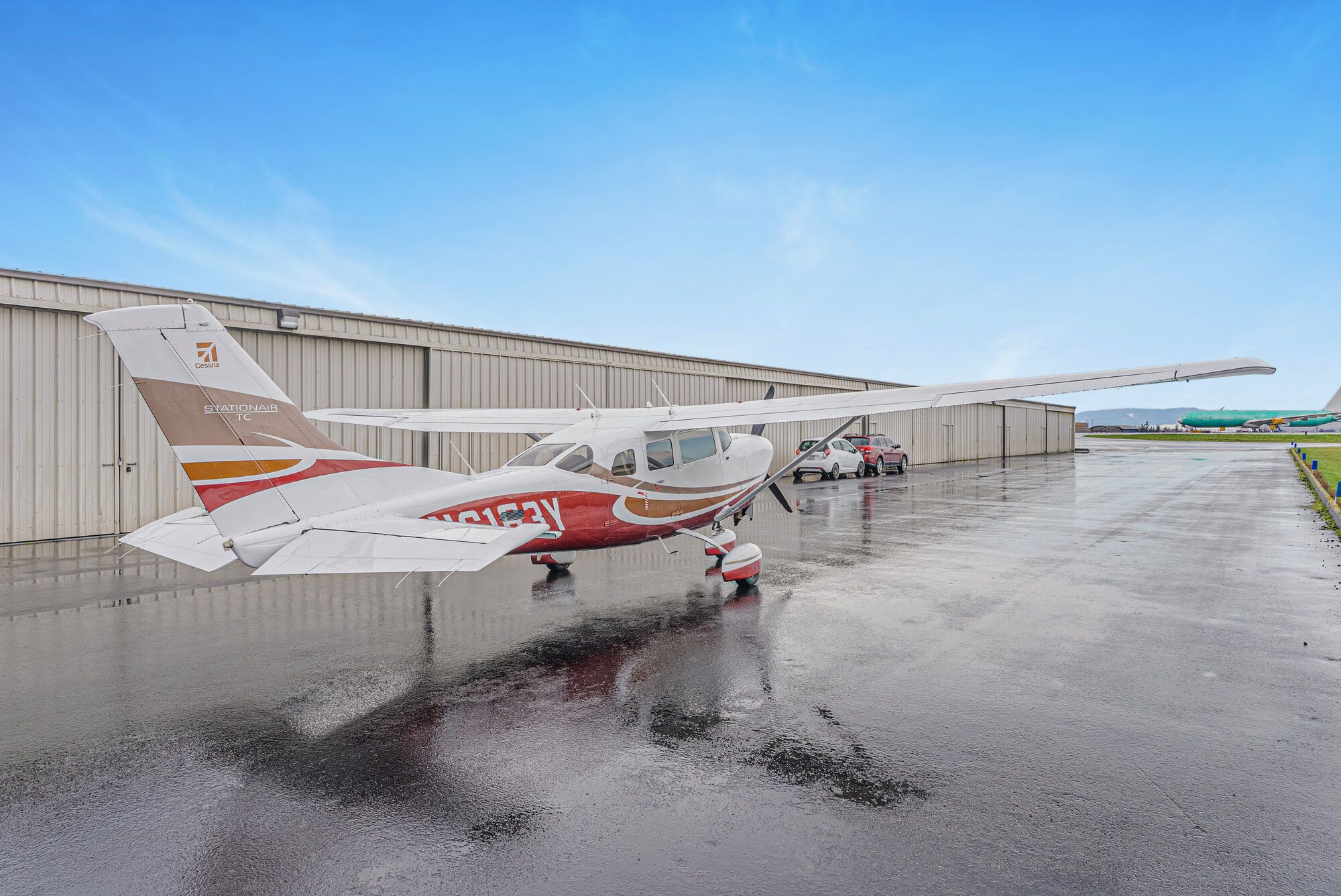 Cessna Turbo Stationair from the rear left on a wet ramp beside a hangar