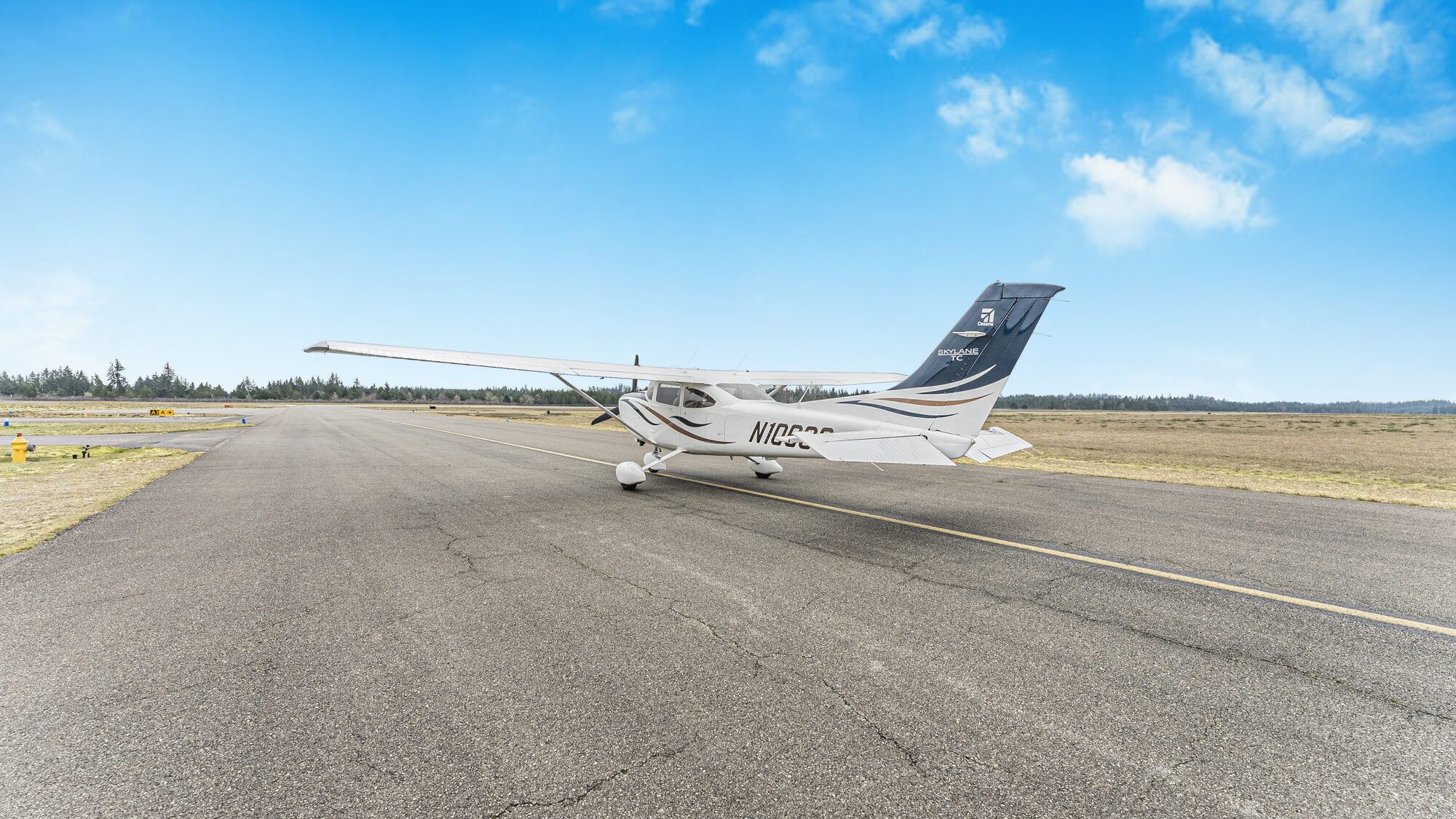 Cessna Turbo Skylane from behind on the taxiway, grass and treeline beyond
